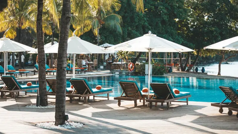 Transats bleus et parasols blancs bordent une piscine turquoise.