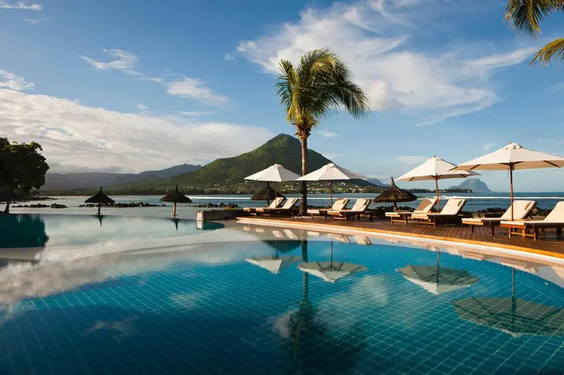 Une piscine à débordement reflète le ciel et la végétation tropicale.