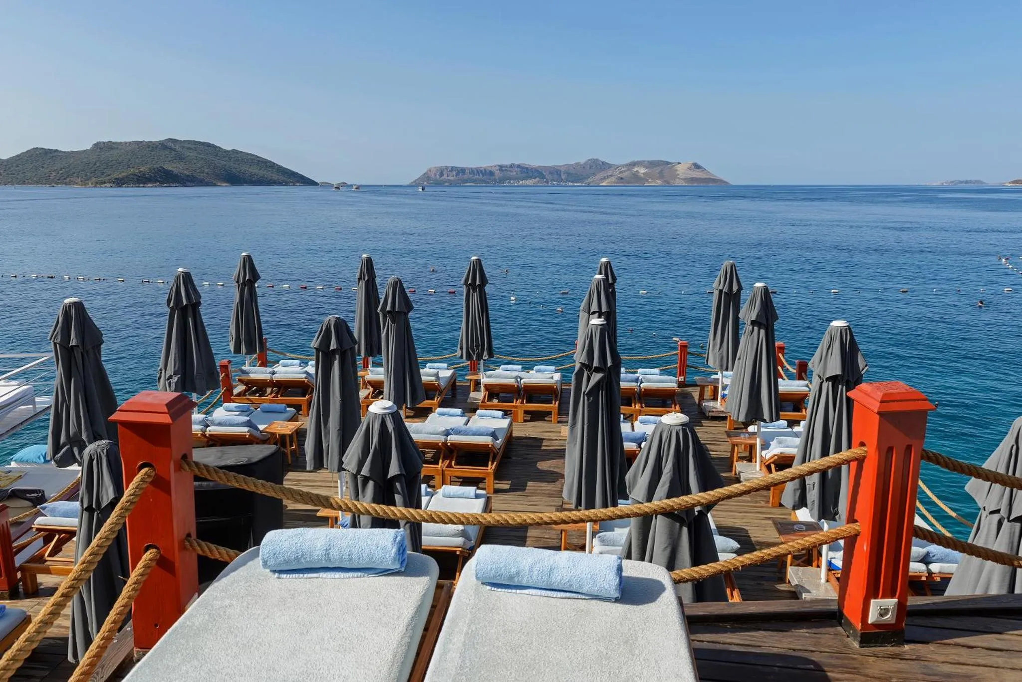 Terrasse en bois avec transats et parasols face à la mer.
