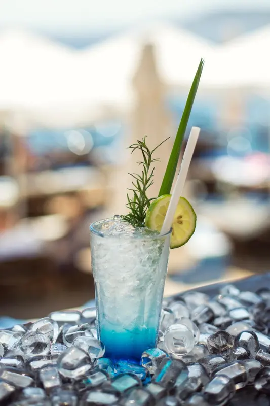 Un cocktail bleu rafraîchissant est servi avec une décoration de romarin et de citron vert.