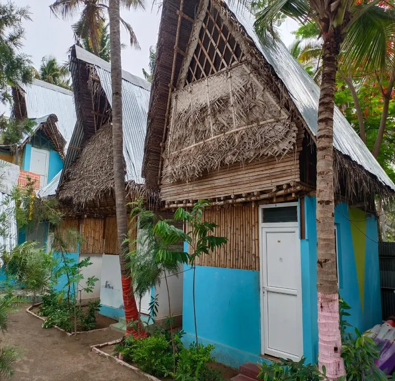 Petites cabanes colorées aux toits de chaume se dressent dans un jardin tropical.