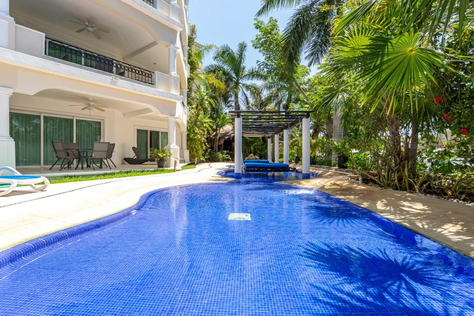 Une piscine turquoise bordée de végétation luxuriante et de transats.
