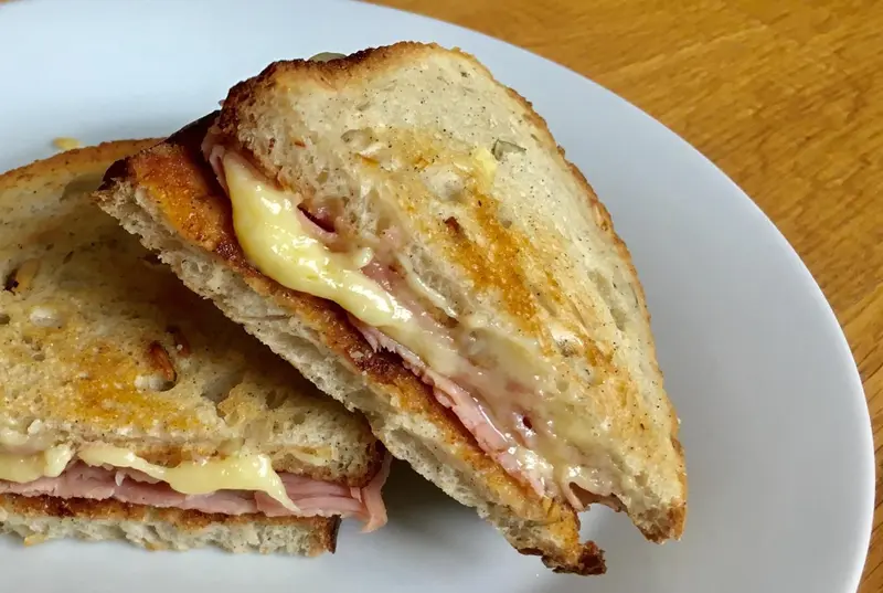 Deux moitiés d'un sandwich chaud au jambon et au fromage fondu sont présentées sur une assiette.