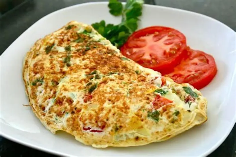 Une omelette aux herbes et aux tomates est présentée sur une assiette blanche.