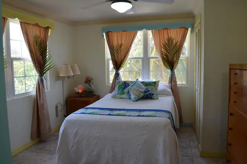Une chambre lumineuse avec un lit recouvert d'une courtepointe colorée et des rideaux aux motifs tropicaux.