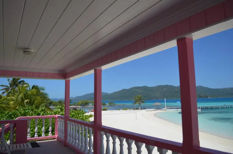 Vue sur une plage de sable blanc et une mer turquoise depuis une terrasse couverte.