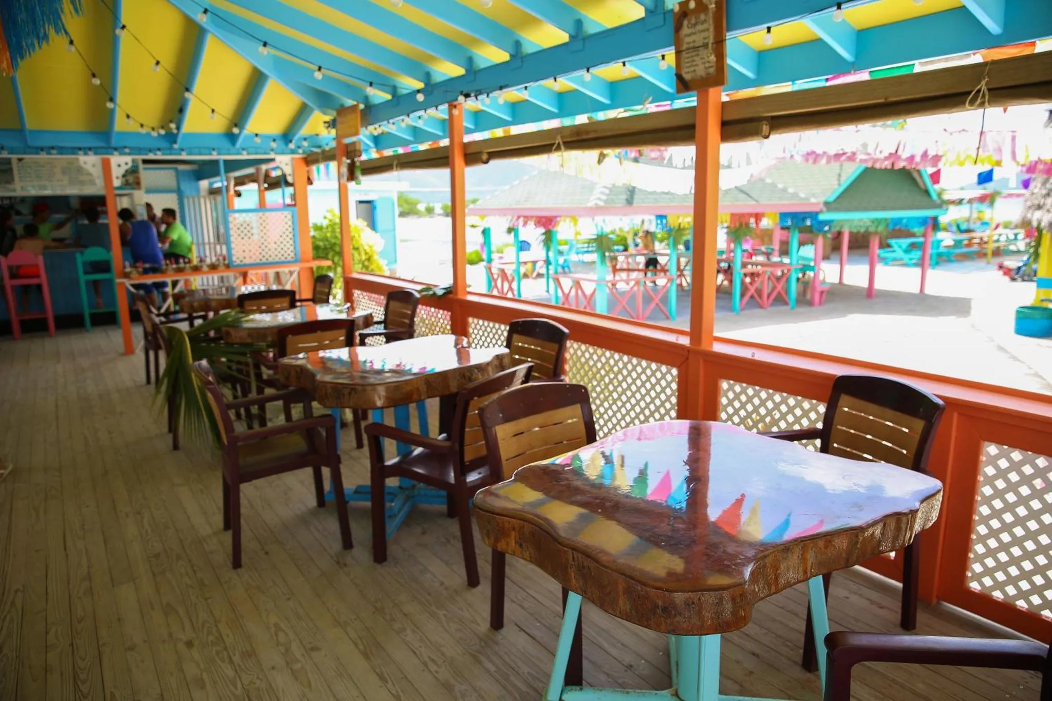 Terrasse ombragée avec tables et chaises colorées face à la mer.