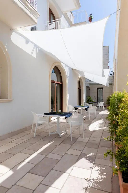 Une cour intérieure ombragée avec des tables et des chaises blanches.