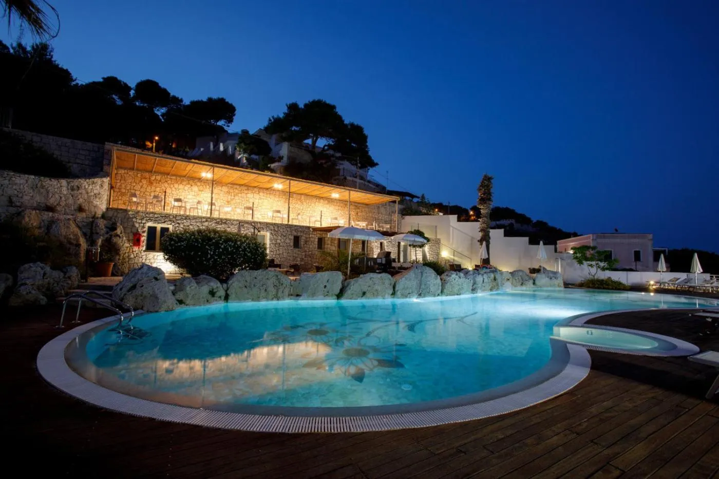 Une piscine illuminée au crépuscule devant un bâtiment éclairé.