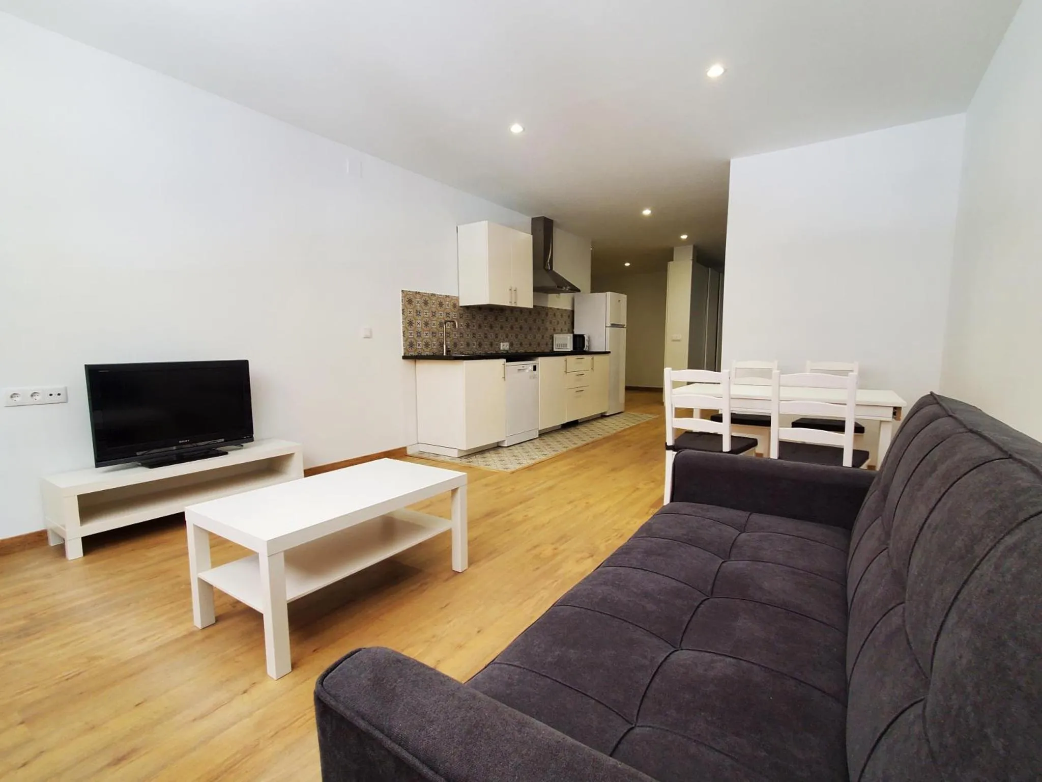 Espace de vie lumineux avec canapé, table basse et cuisine équipée.