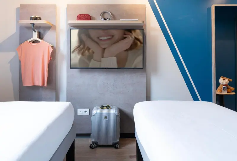 Une chambre avec deux lits et une télévision murale.