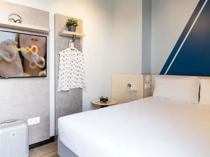 Une chambre lumineuse avec un lit blanc et une télévision murale.
