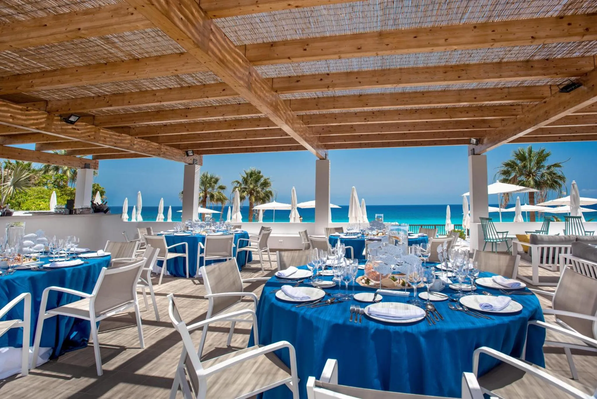 Tables dressées sur une terrasse ombragée face à la mer.