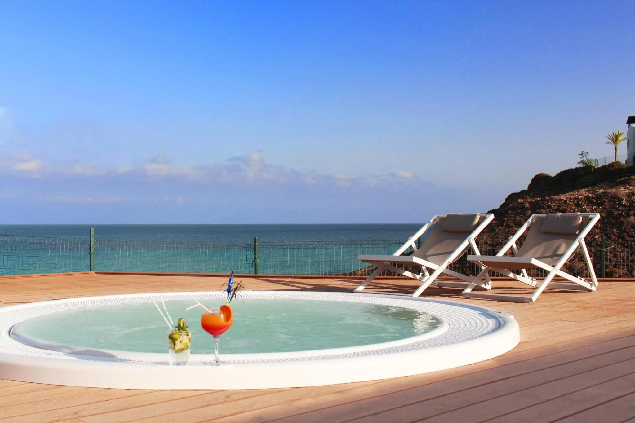 Deux transats et un jacuzzi sur une terrasse en bois avec vue sur la mer.