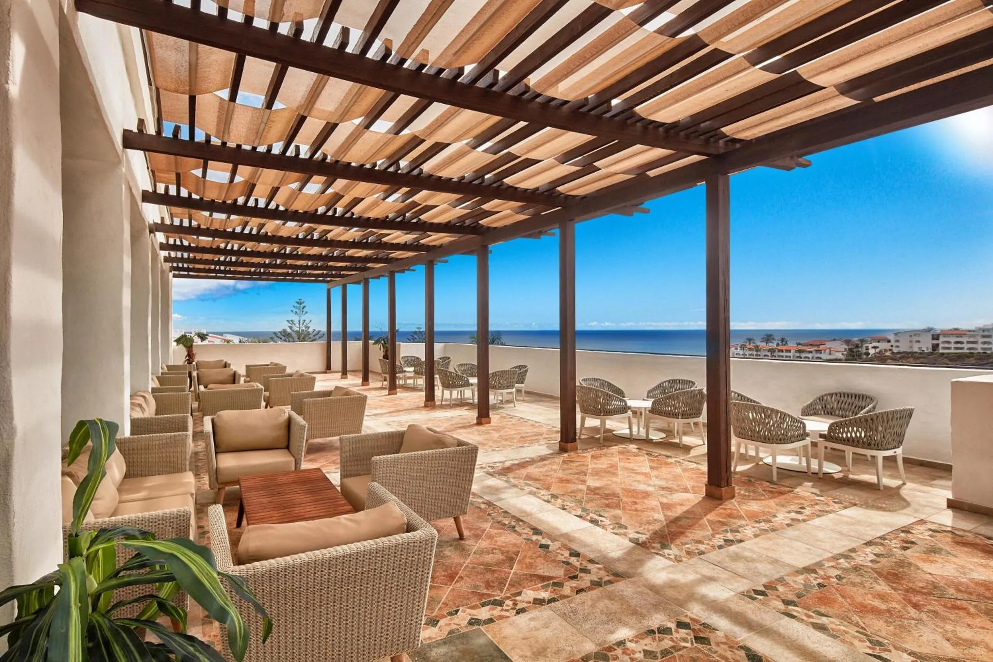 Terrasse ombragée avec mobilier de détente et vue sur la mer.