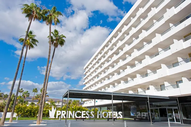 Façade d'un bâtiment blanc avec des balcons et des palmiers devant l'entrée.