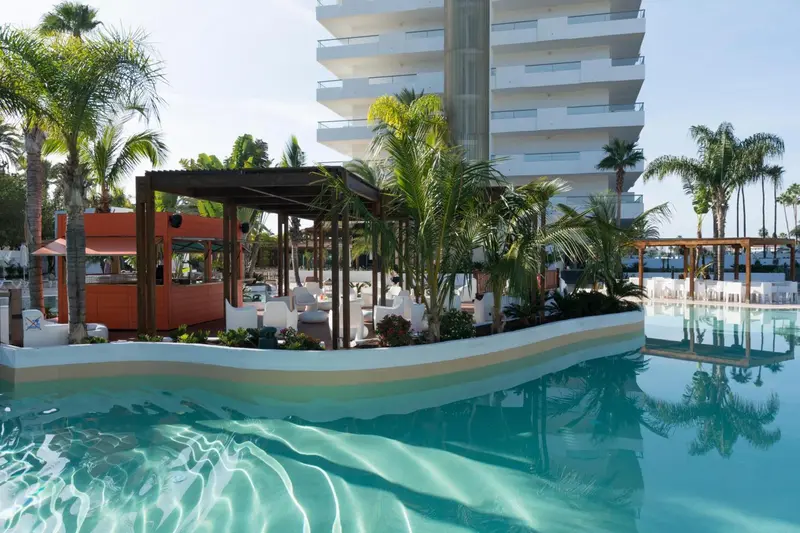 Une piscine turquoise bordée de végétation tropicale et de mobilier blanc.