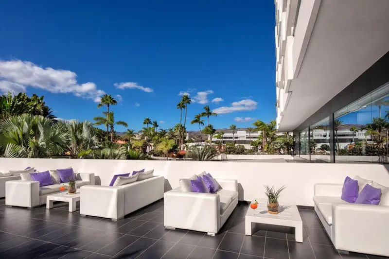Espace de détente extérieur avec mobilier blanc et végétation tropicale.