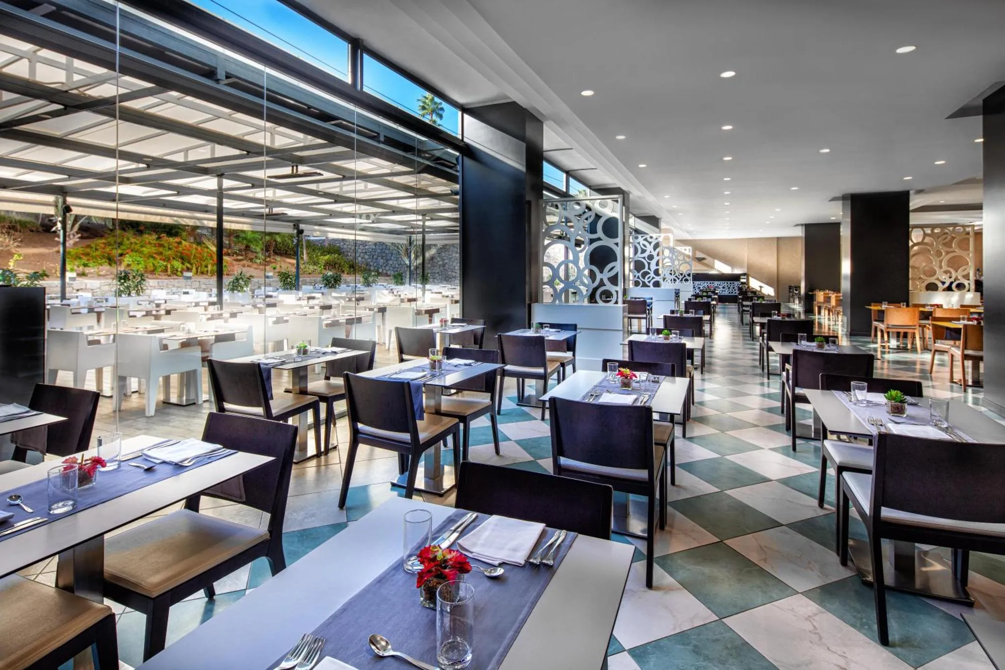 Une salle de restaurant lumineuse avec des tables dressées et un sol à carreaux.