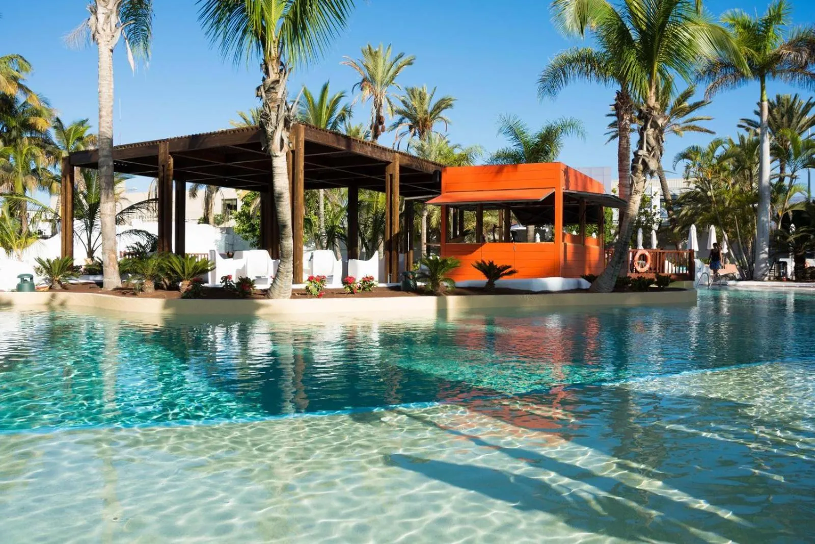 Une piscine turquoise bordée de palmiers et d'une structure ombragée.