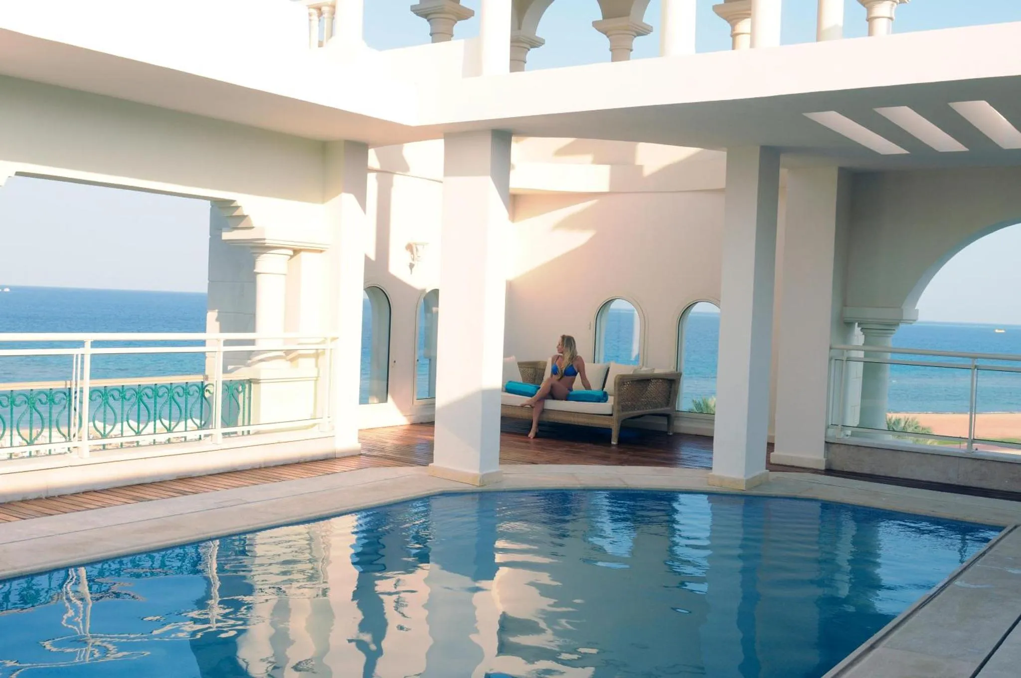 Une femme se détend sur une terrasse avec vue sur la mer et une piscine.