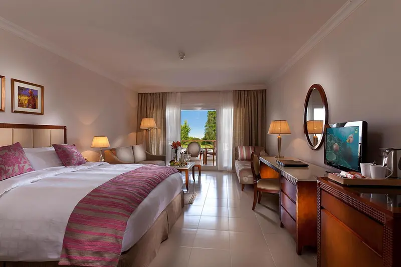 Une chambre lumineuse avec un grand lit et un coin salon donnant sur une vue extérieure.