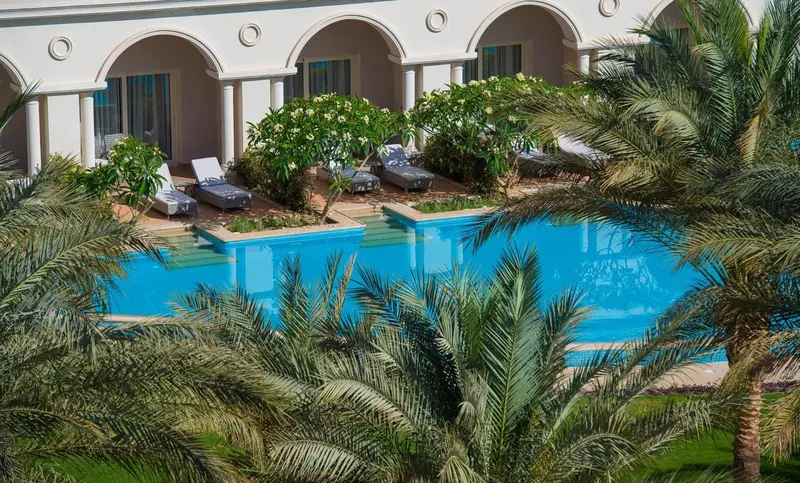 Transats alignés au bord d'une piscine turquoise dans un jardin tropical.