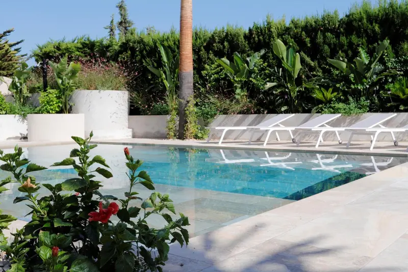 Transats blancs alignés au bord d'une piscine rectangulaire turquoise.