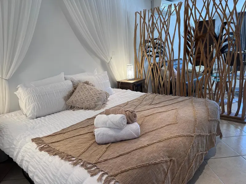 Un lit king-size est recouvert d'une couverture texturée et de coussins décoratifs dans une chambre lumineuse.