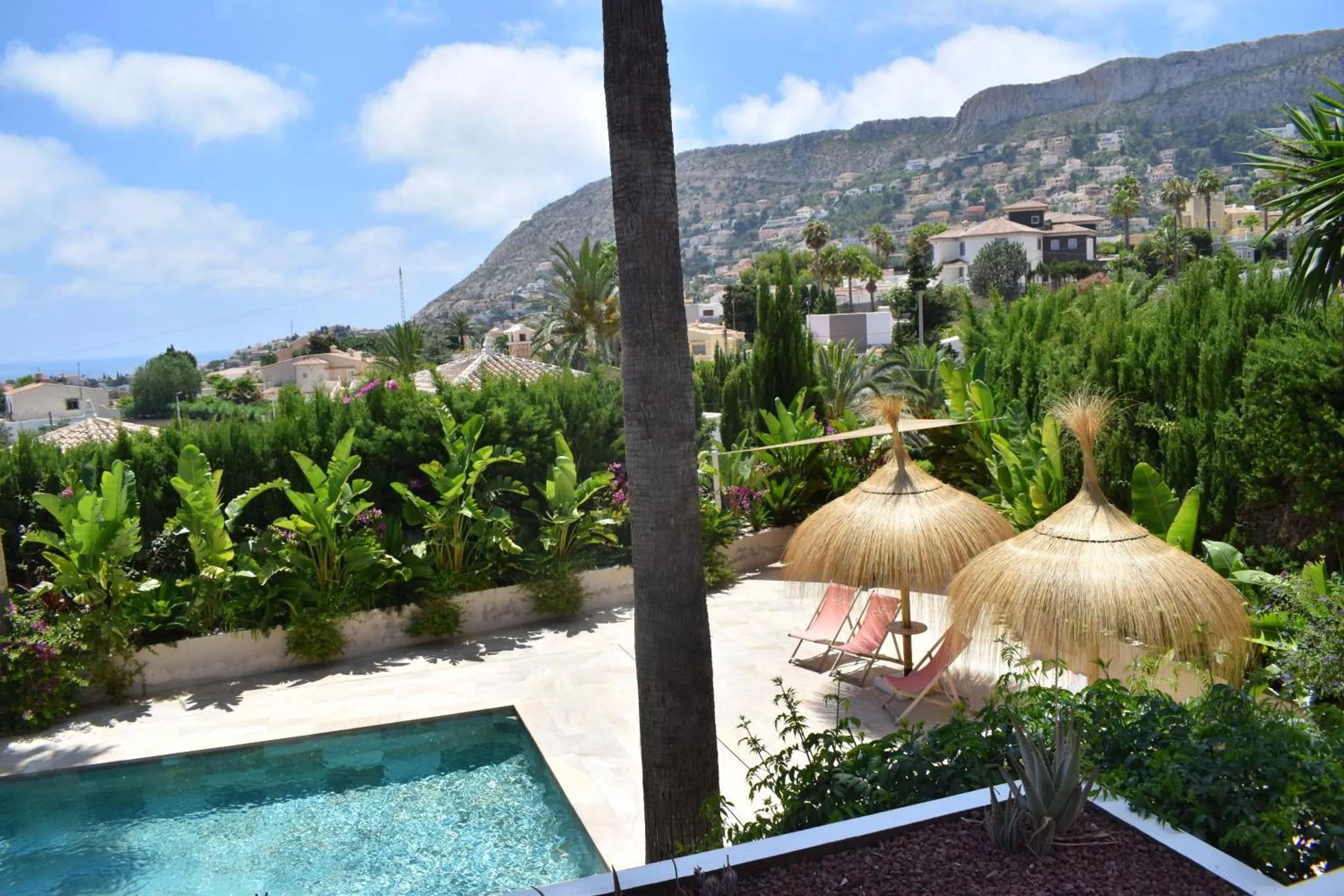 Deux transats ombragés par des parasols en chaume bordent une piscine turquoise.