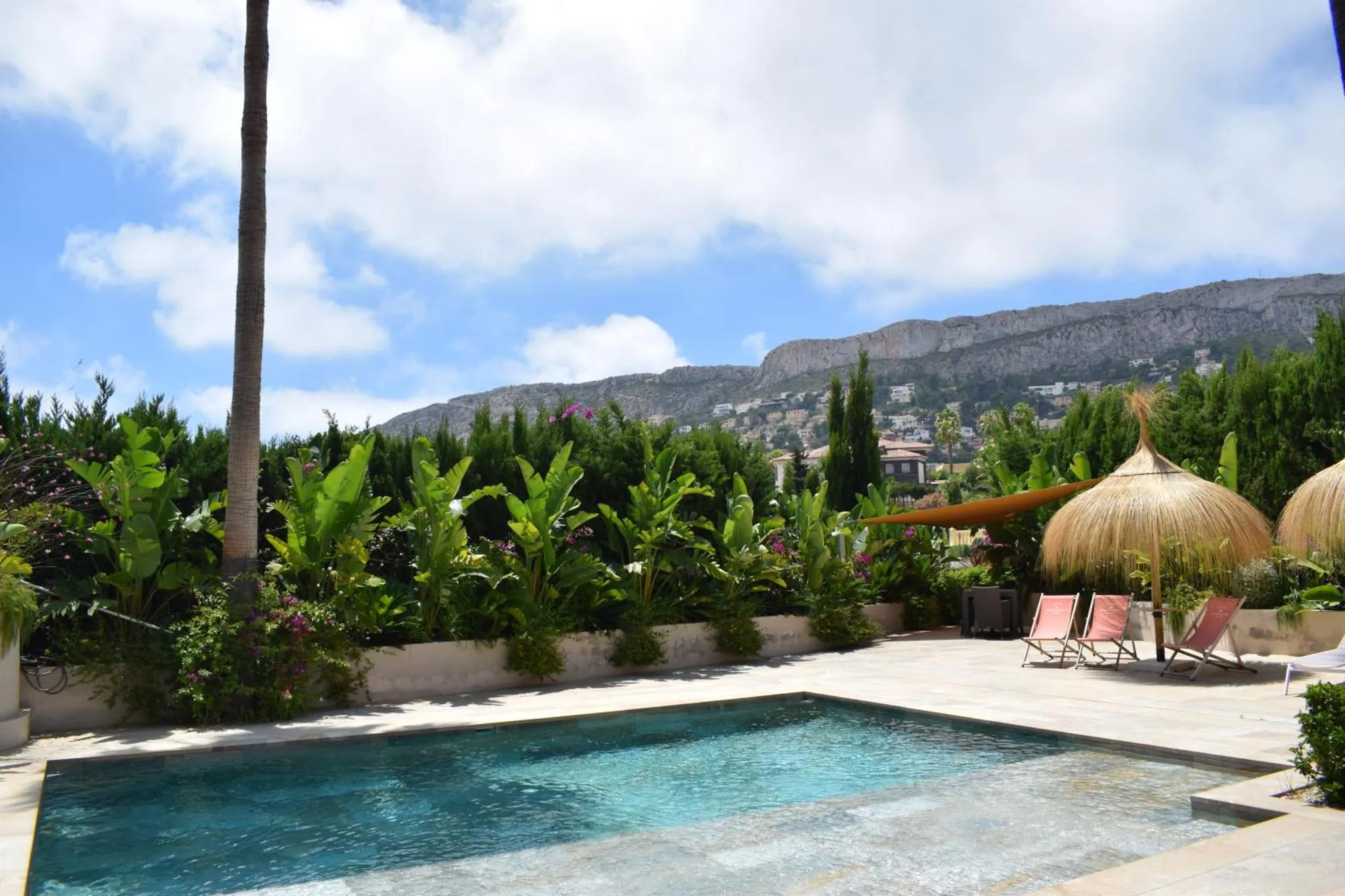 Une piscine rectangulaire bordée d'une terrasse ensoleillée avec des transats et des parasols.