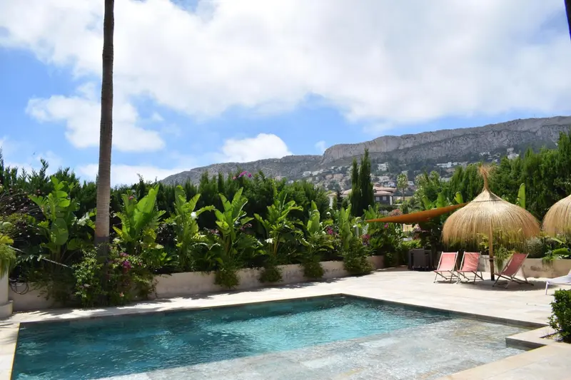 Une piscine rectangulaire bordée d'une terrasse ensoleillée avec des transats et des parasols.