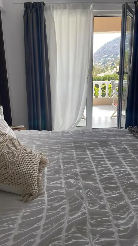 Lit blanc avec coussins dans une chambre donnant sur une terrasse et un paysage montagneux.