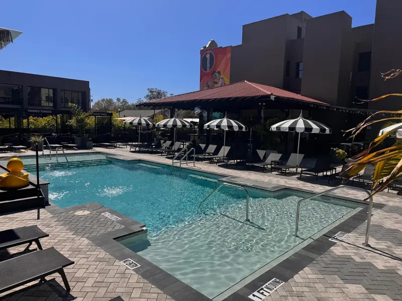 Une piscine rectangulaire bordée de chaises longues et de parasols rayés.