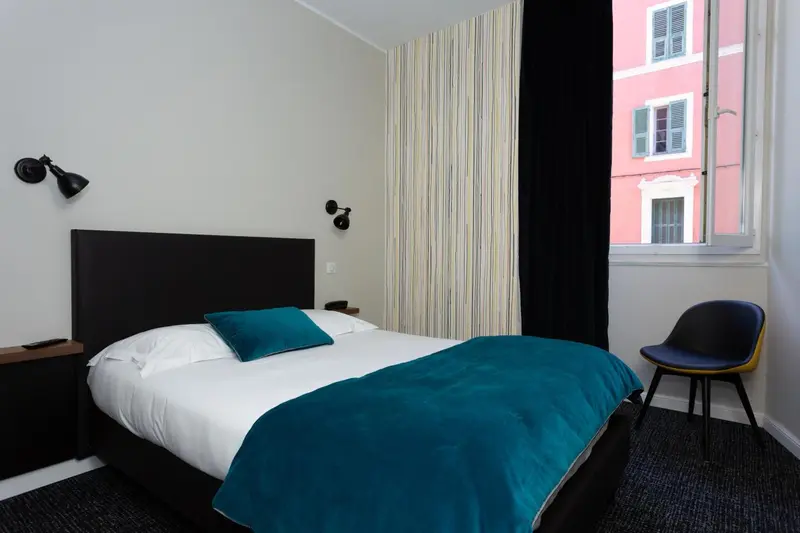 Une chambre lumineuse avec un lit recouvert d'une couverture turquoise et une chaise.