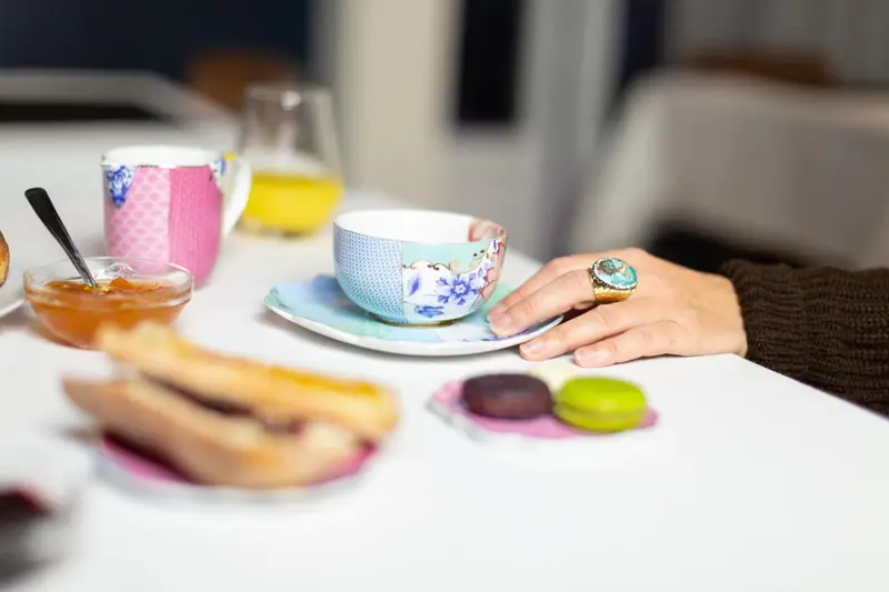 Une main tenant une tasse à thé sur une table avec des pâtisseries et de la confiture.