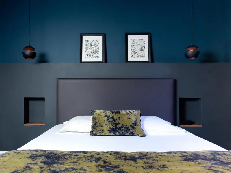 Un lit recouvert d'une courtepointe décorative se trouve devant un mur sombre orné de cadres.