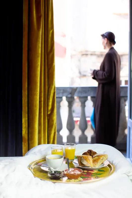 Un petit-déjeuner est servi sur un plateau devant une fenêtre ouverte sur un balcon.