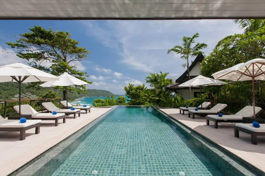 Transats et parasols bordent une piscine à débordement avec vue sur la mer.