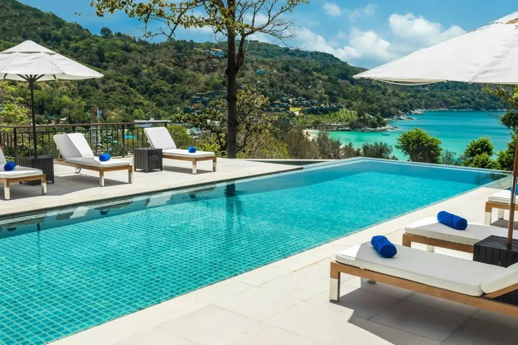 Transats et piscine avec vue sur la mer et la végétation.