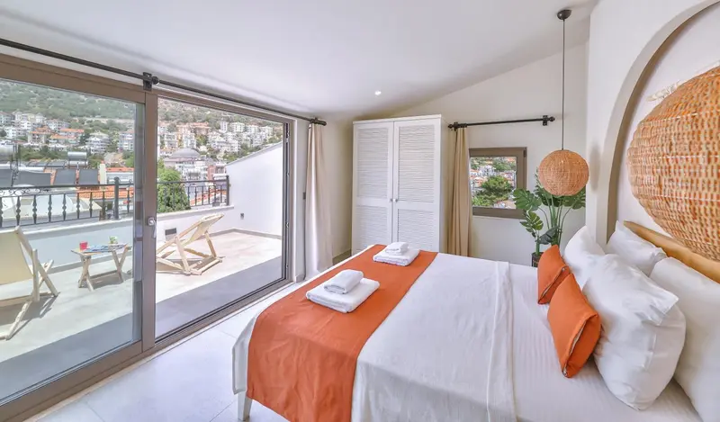 Chambre lumineuse avec un lit recouvert d'une courtepointe orange et un accès à une terrasse.