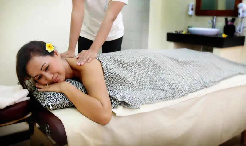 Une femme reçoit un massage sur une table de soin dans une pièce lumineuse.