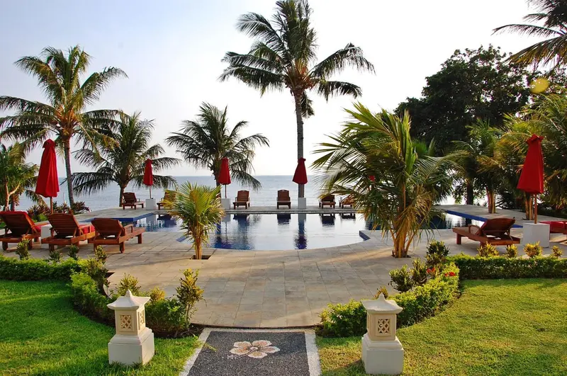 Une piscine rectangulaire bordée de chaises longues et de végétation tropicale.