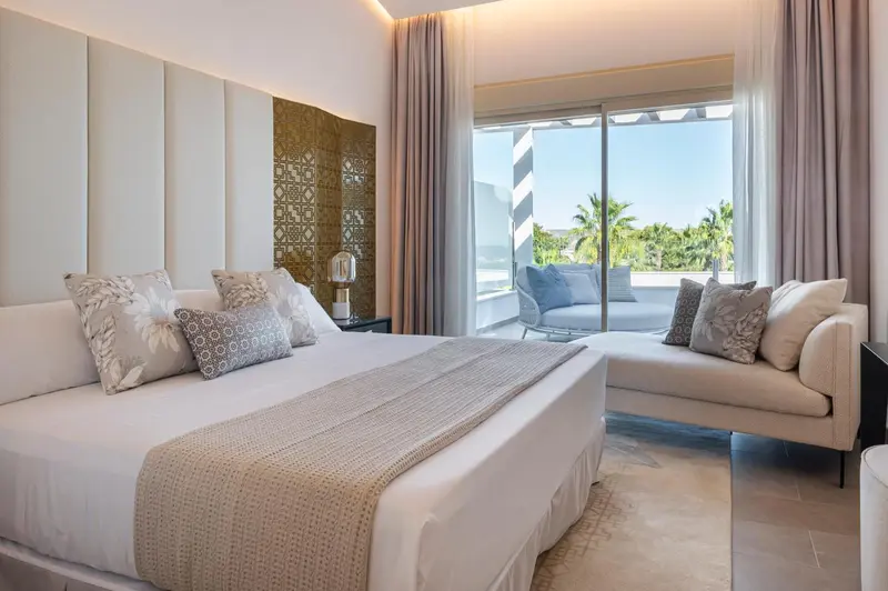 Une chambre lumineuse avec un grand lit et un coin salon donnant sur une terrasse.