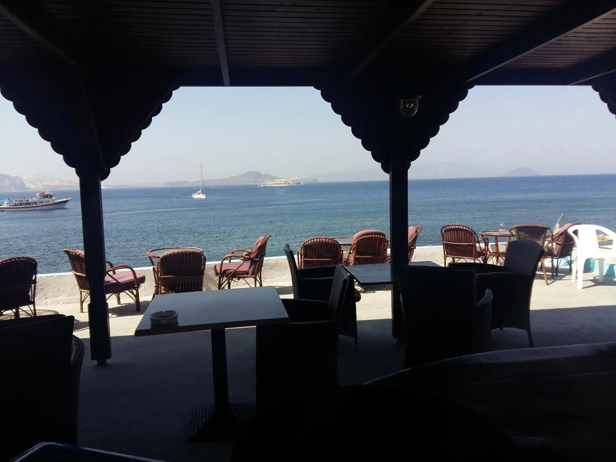 Terrasse ombragée donnant sur la mer et des bateaux.