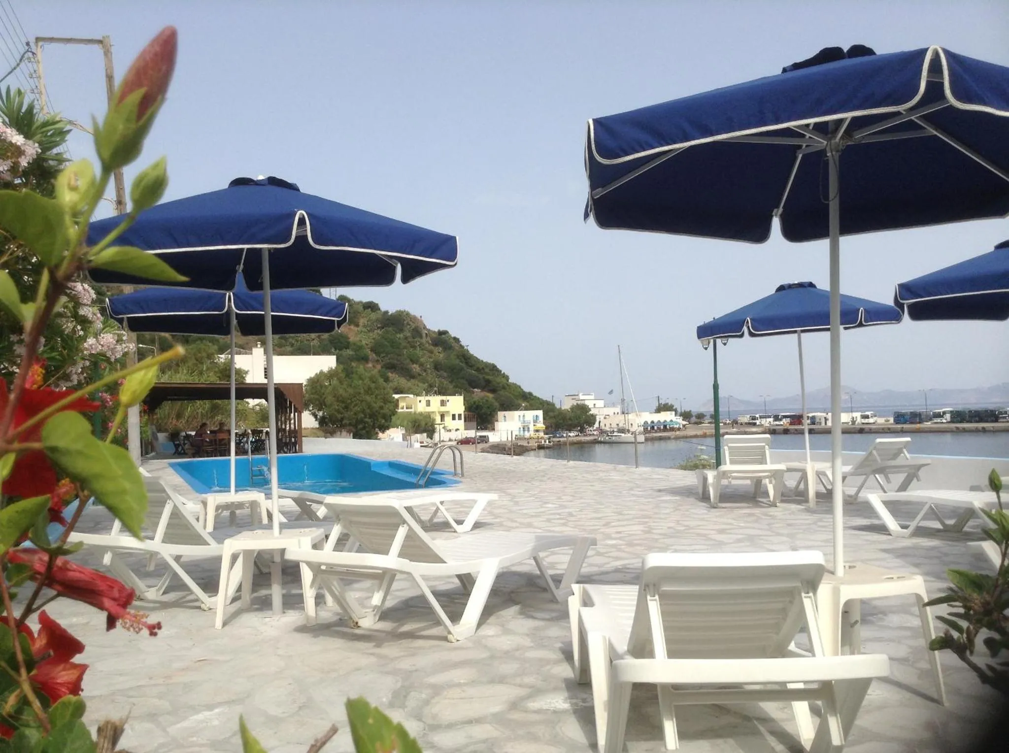 Transats blancs disposés autour d'une piscine en bord de mer sous des parasols bleus.