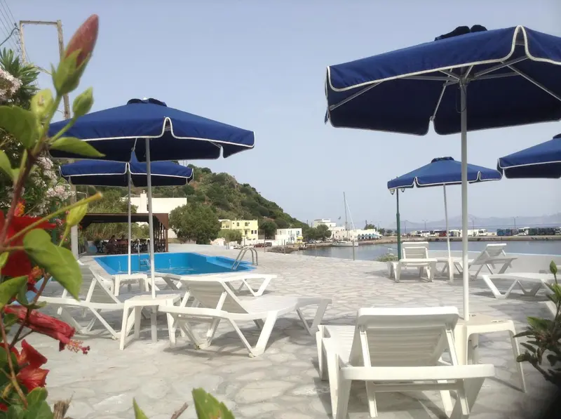 Transats blancs disposés autour d'une piscine en bord de mer sous des parasols bleus.