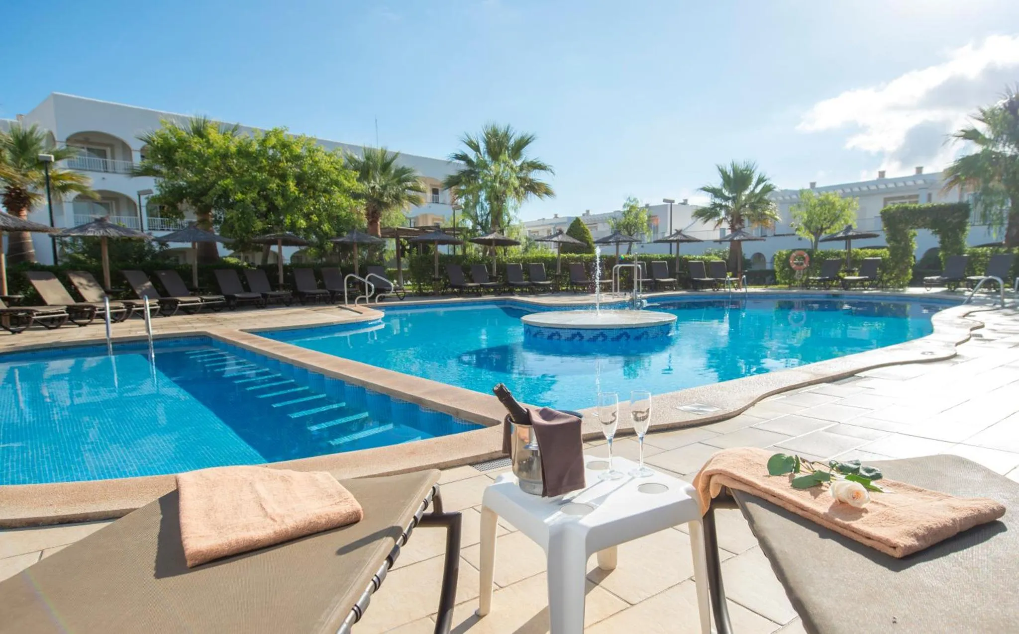 Deux transats avec des serviettes et une table basse près d'une piscine ensoleillée.
