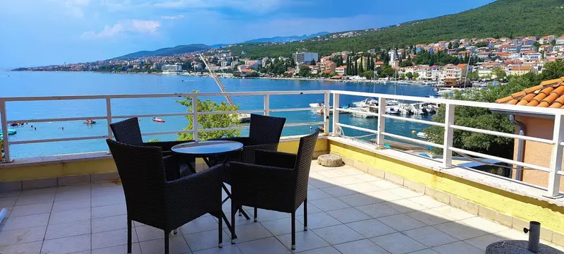 Terrasse avec mobilier de jardin donnant sur une vue mer et une ville côtière.
