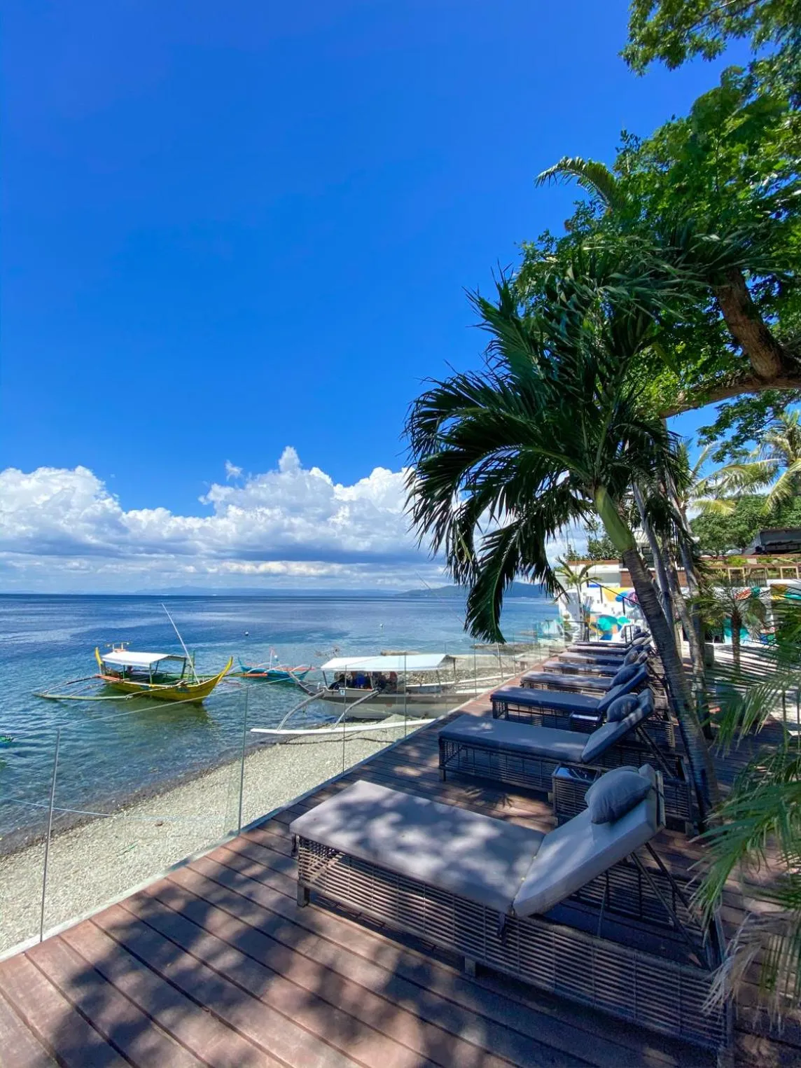 Terrasse en bois avec transats face à la mer et à des bateaux.